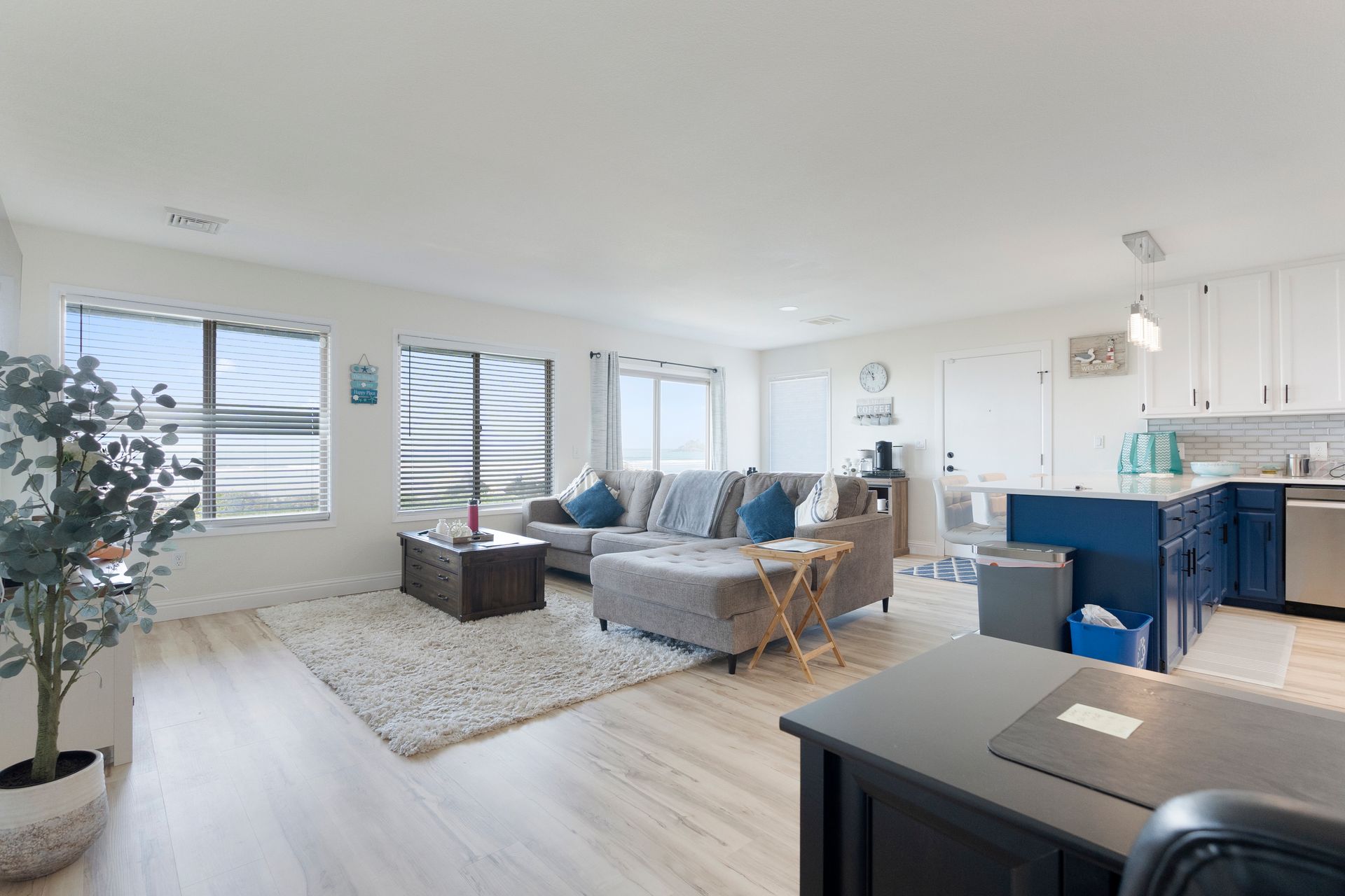 Open-concept living space with a blue sectional, white walls, and a kitchen with navy cabinets.