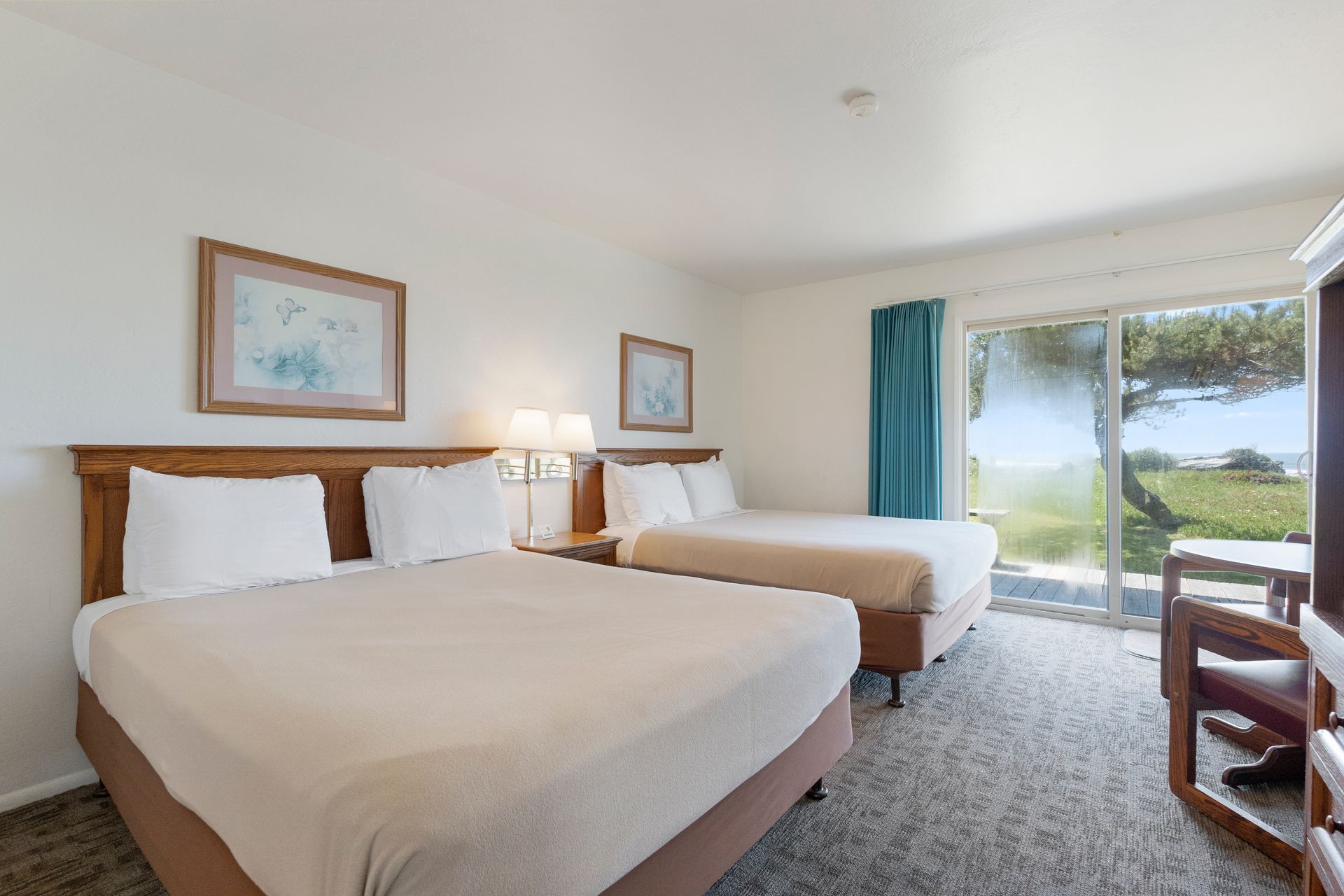 A motel room with two beds, a table, and a sliding glass door to an outdoor view.