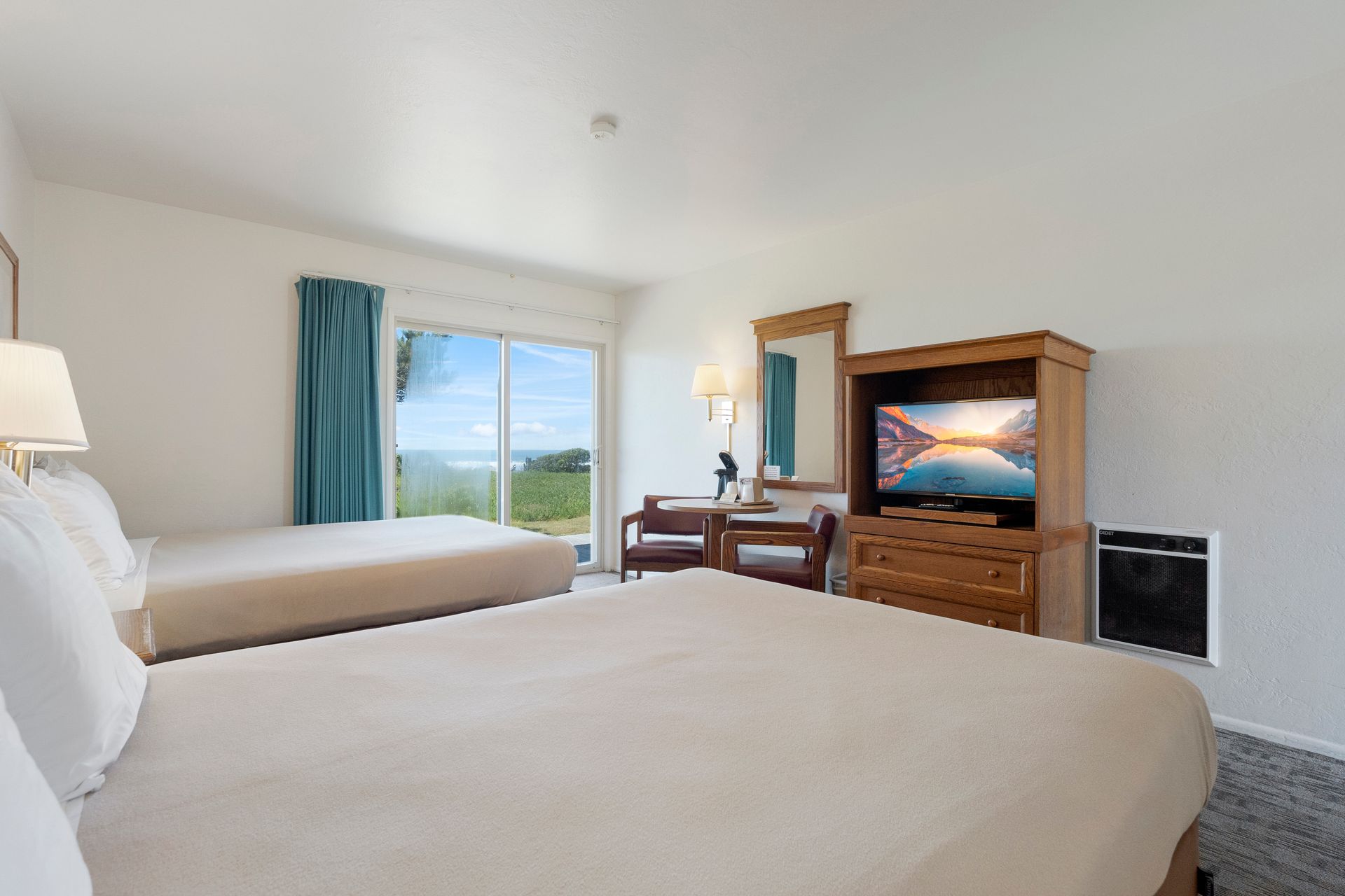 Hotel room with two beds, TV, and window overlooking a green landscape.