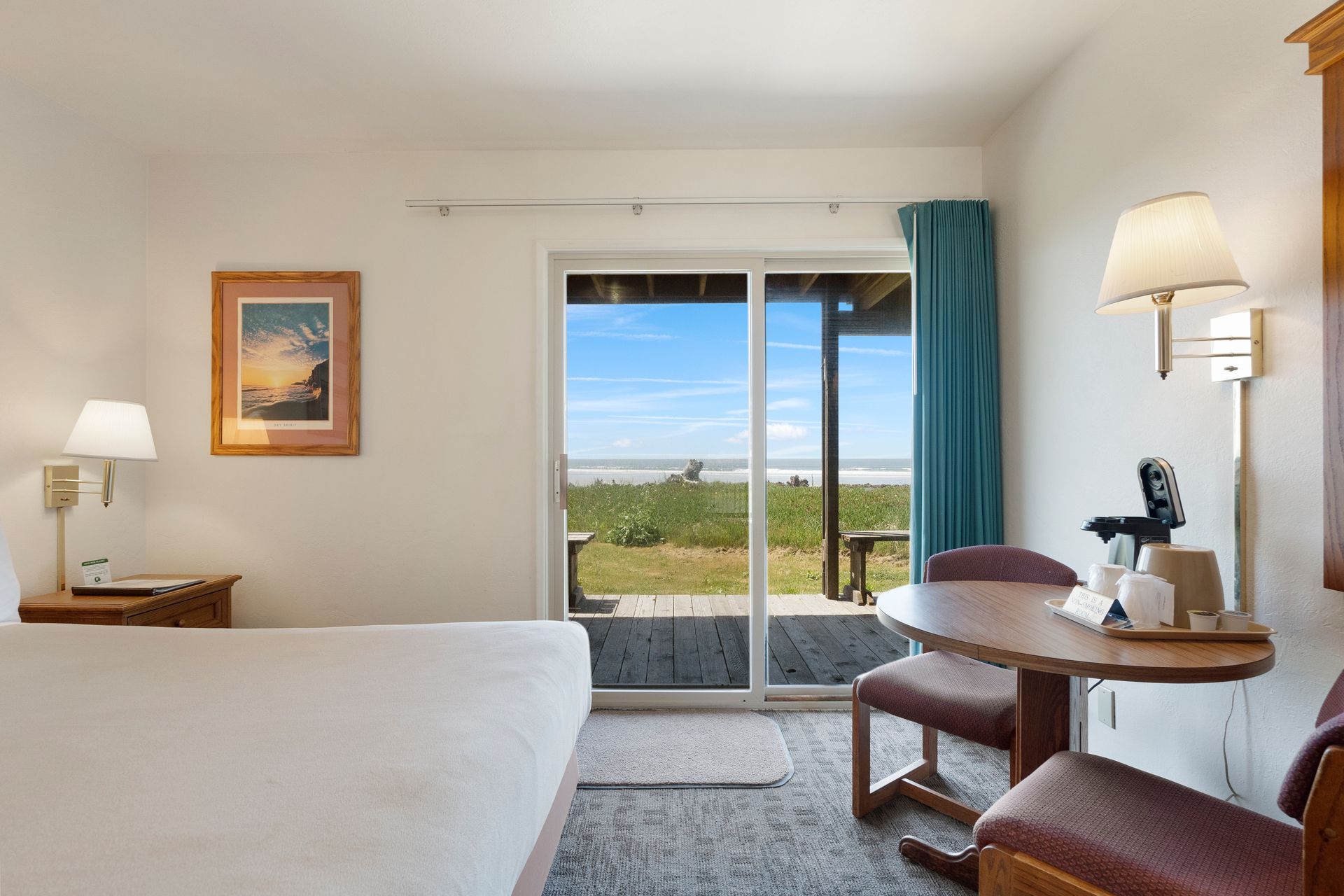 Hotel room with ocean view: bed, table, chairs, open sliding glass door to beach.