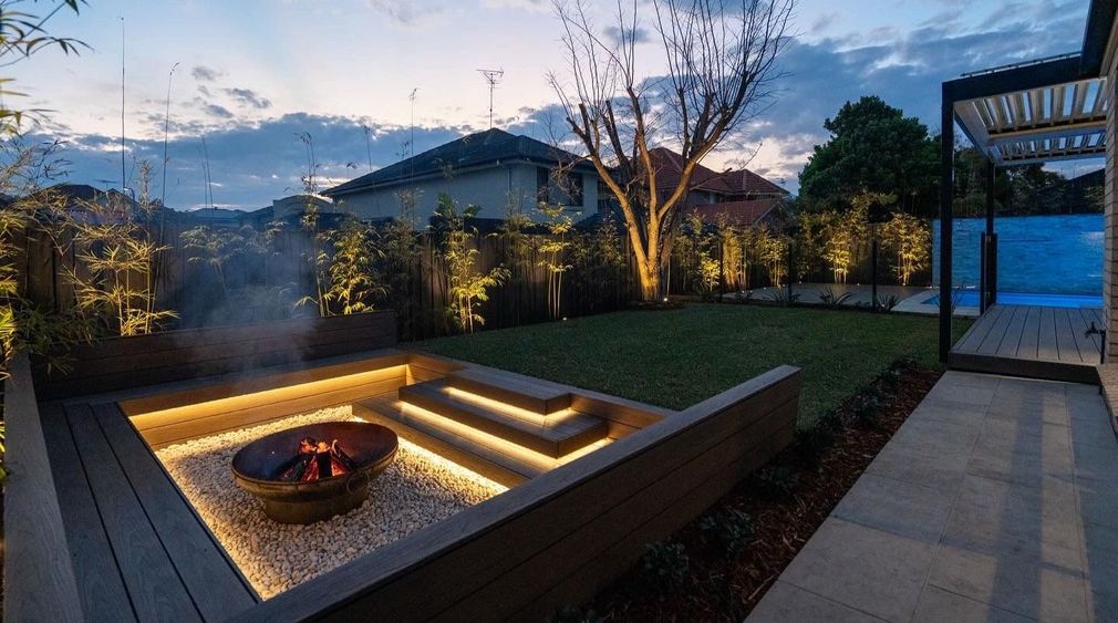 A sunken fire pit with feature lighting, surrounded by bamboo.
