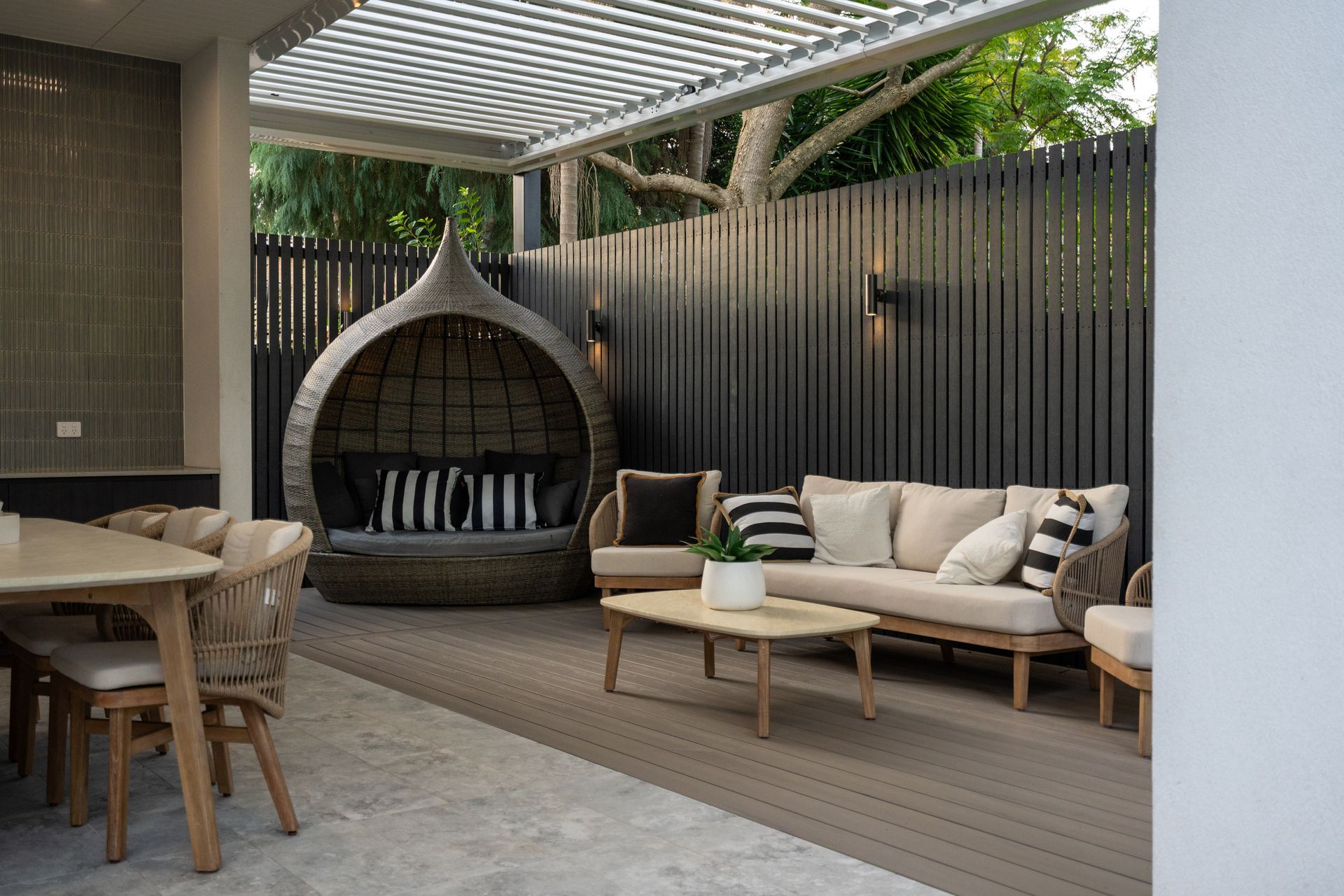 A patio with a couch , chairs , a table and a motorised pergola.