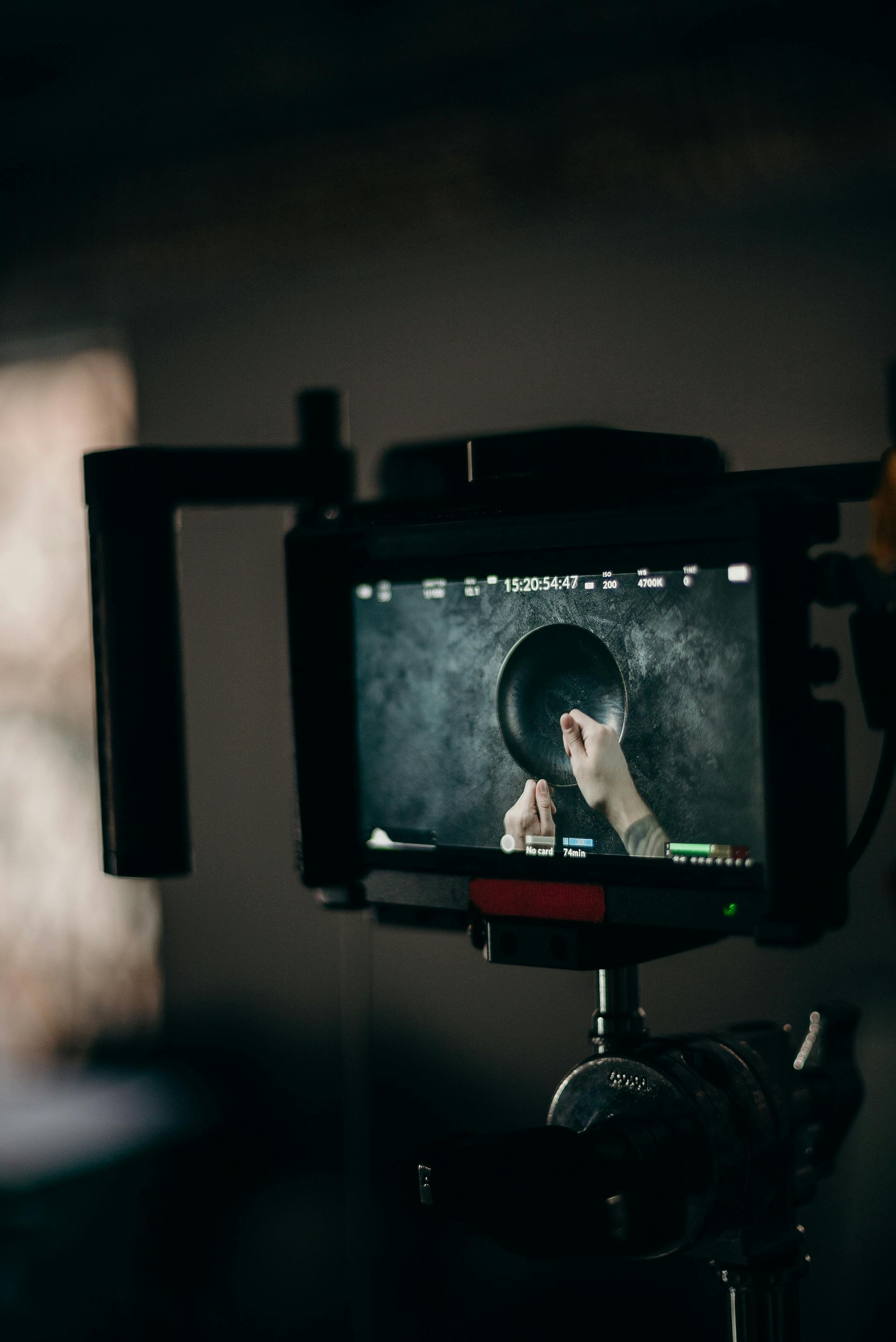 Camera filming hands holding a pan in a dark kitchen, reflected in the monitor.