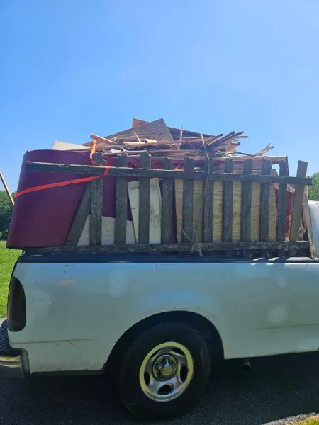 White pickup truck bed loaded with debris, secured with a red strap under a bright blue sky.
