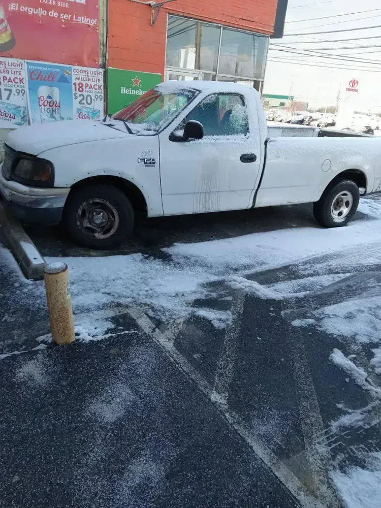 White pickup truck parked on snow-covered pavement in front of a convenience store.