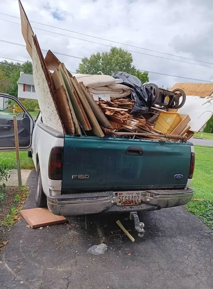 Green Ford F-150 truck bed overflowing with construction debris on a driveway.
