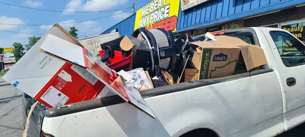A white pickup truck bed overflowing with boxes and other items in front of a business.