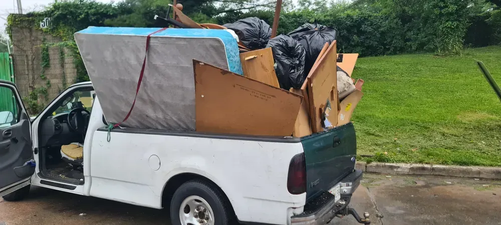 White pickup truck overflowing with debris and a mattress, parked outdoors.