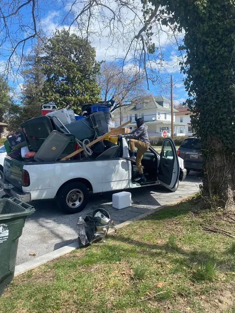A person loads a white pickup truck overflowing with items on a sunny street.