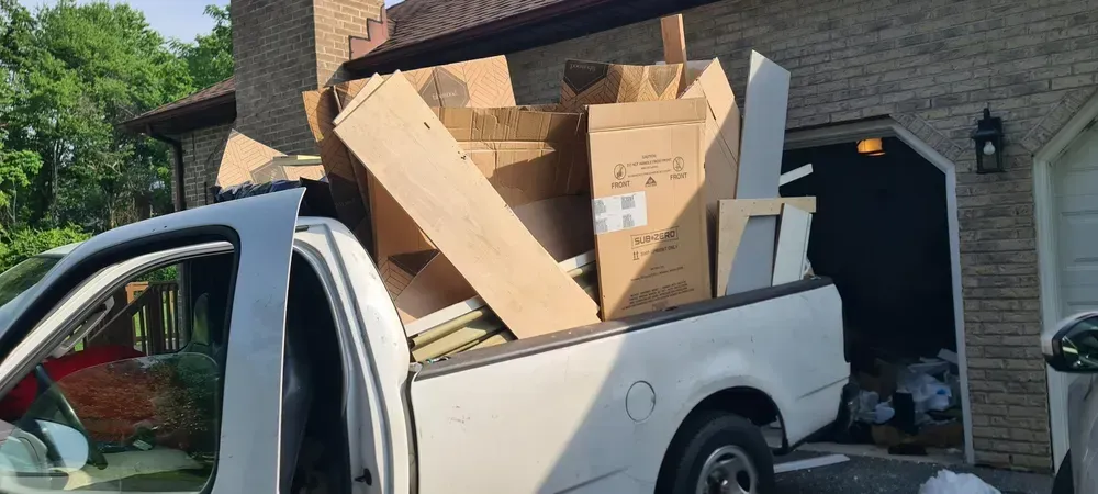 A white pickup truck overloaded with cardboard boxes and furniture in front of a house.
