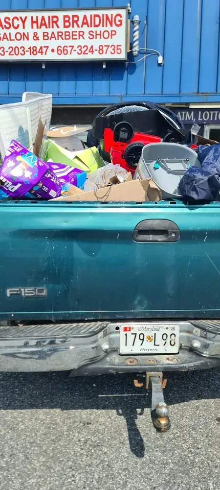 A green pickup truck bed filled with items parked in front of a hair braiding salon.