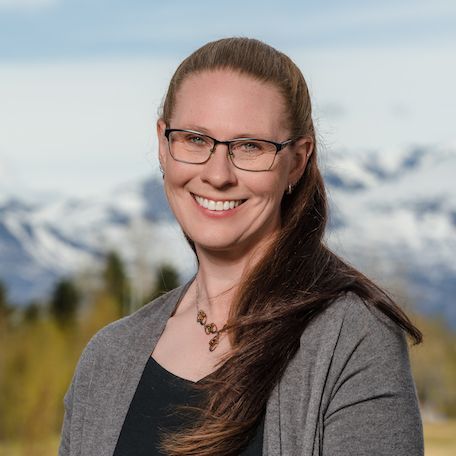 Woman with glasses smiles; mountains in background.