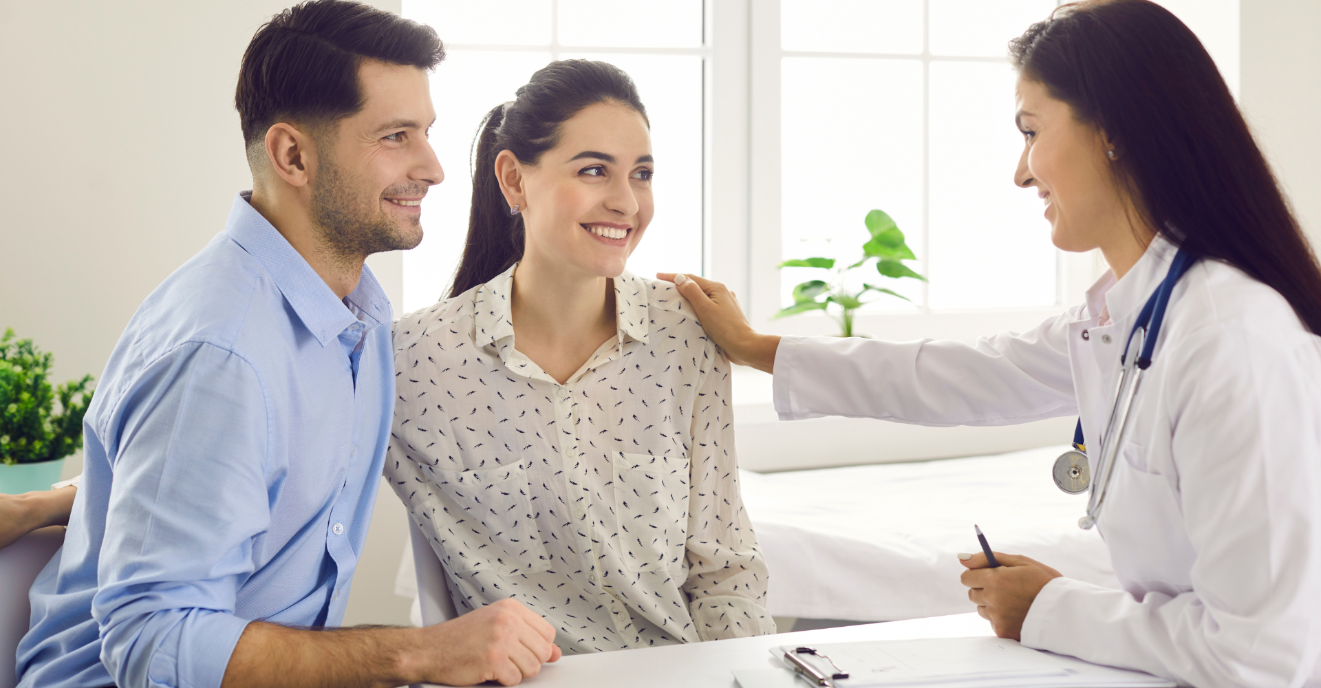 Couple smiling at a doctor, who has a hand on the woman's shoulder. They are in an office setting.