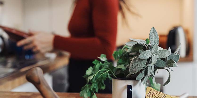 Fresh herbs in a mug on a kitchen counter, with a person blurred in the background.