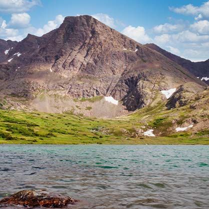 Mountain landscape with a turquoise lake, green grass, and snow patches.