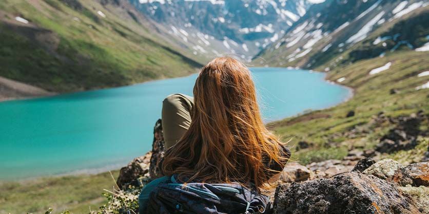 Woman with red hair overlooking a turquoise lake surrounded by mountains.