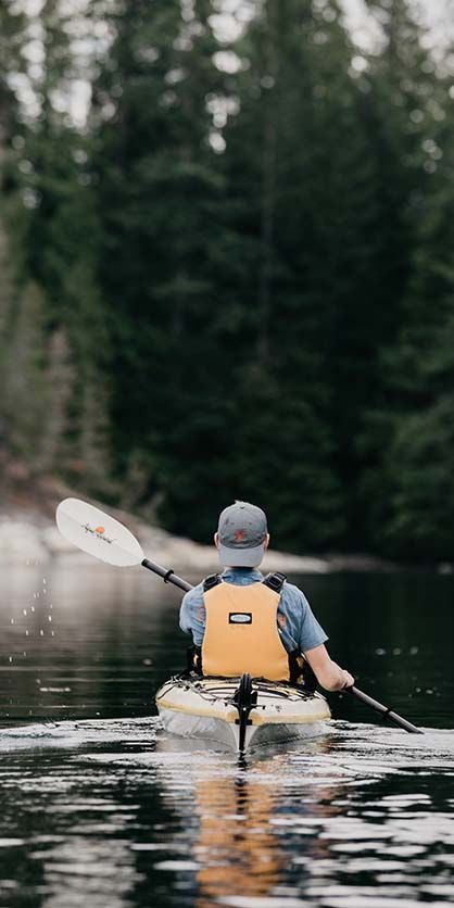 Person kayaking on a lake with a forest background.
