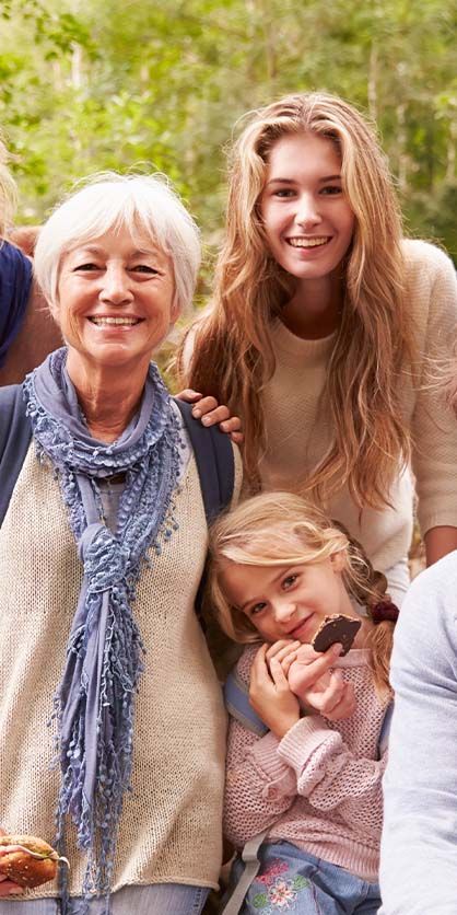 Family portrait, outdoors. Woman with white hair smiles, next to a young woman, and a child eating a treat.