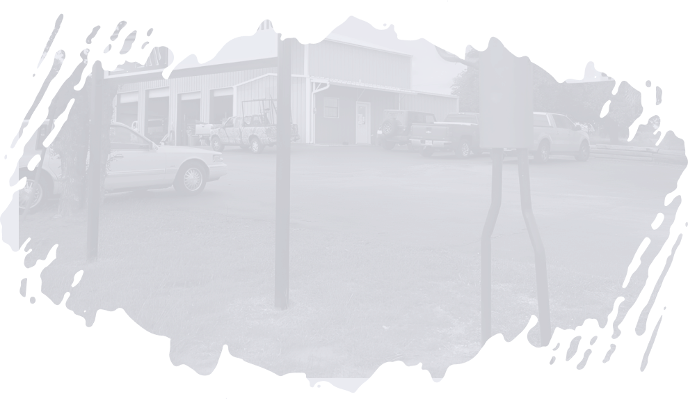 A blurred, light-colored building with a fence in front. Vehicles parked nearby. | Do Good Automotive