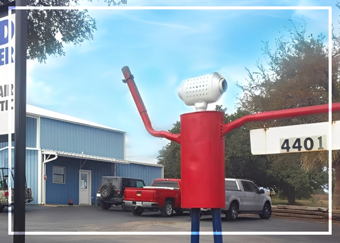 Red metal figure with arms outstretched in front of a blue building, sign says 4401, blue sky. | Do Good Automotive