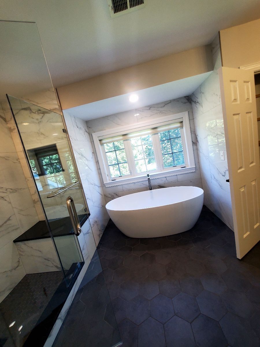 Modern bathroom with freestanding tub, glass shower, dark floor, and window light