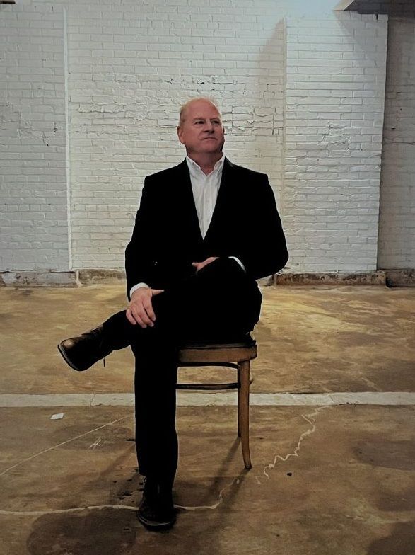A man in a suit is sitting on a chair with his legs crossed