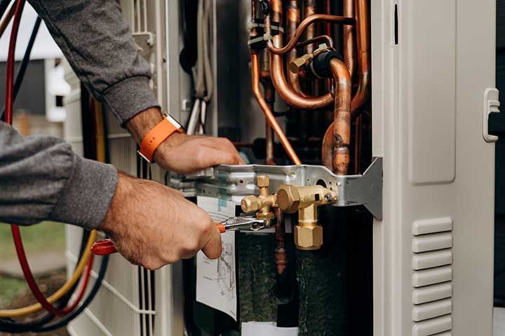 Technician's hands with tools working on the copper pipes of the air conditioner.