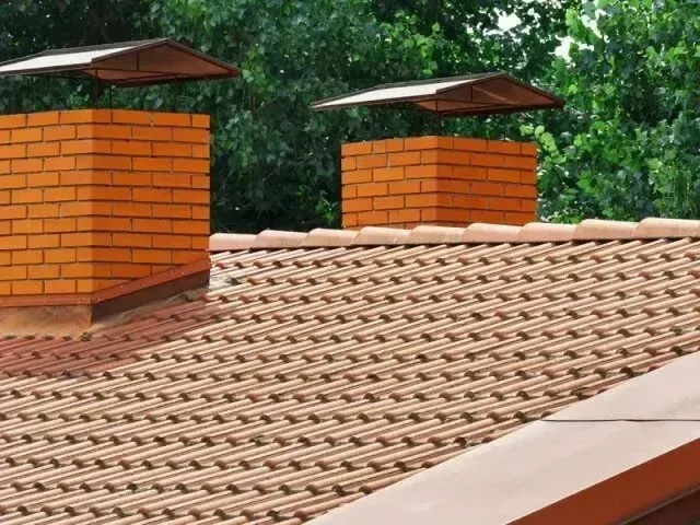 Chimney-Sweep-Portland - Chimney-Sweep-Portland - Two brick chimneys with protective caps rise above a tan tiled roof.