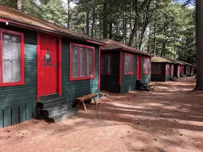 Chimney-Sweep-Portland-Row of rustic, green and red-painted cabins with numbered doors nestled among tall trees. Sunny day, dirt pathway, tranquil and inviting atmosphere.