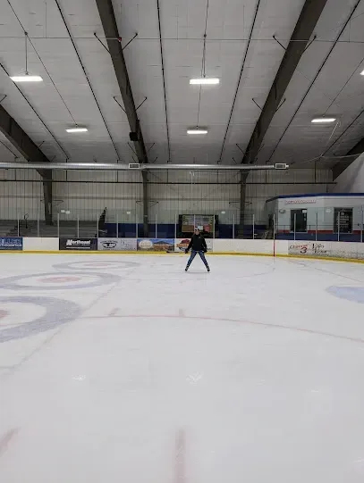 Chimney-Sweep-Portland-A solitary figure ice skates on a rink under a high, industrial ceiling with bright overhead lights.
