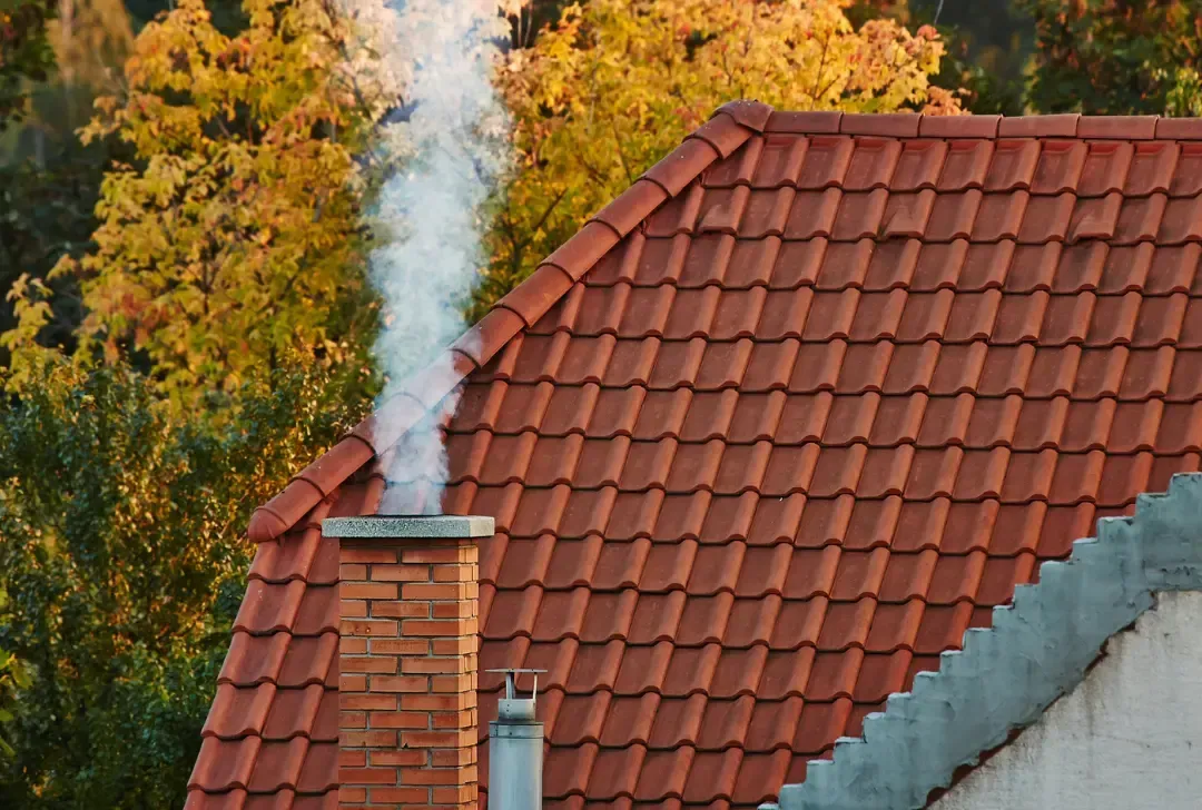 Smoke is coming out of a chimney on the roof of a house.