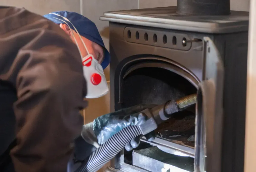 A man wearing a mask is cleaning a fireplace with a vacuum cleaner.