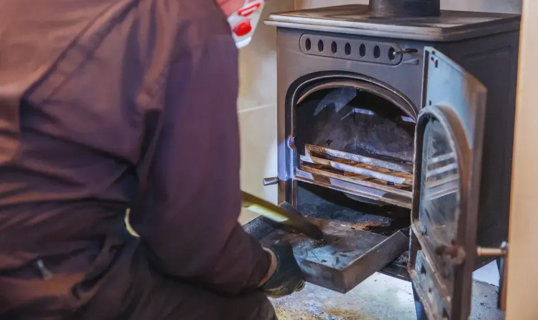 A man is cleaning a wood stove with a shovel.