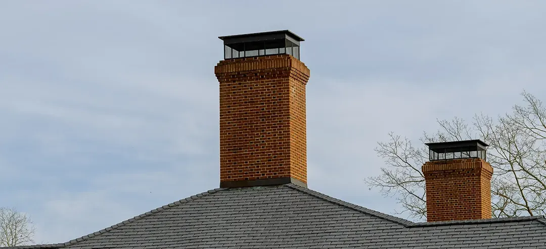 There are two chimneys on the roof of a house.