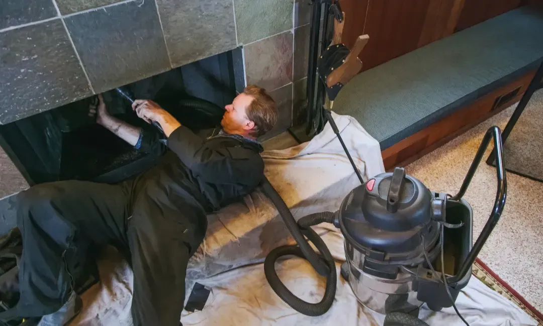 A man is cleaning a fireplace with a vacuum cleaner.