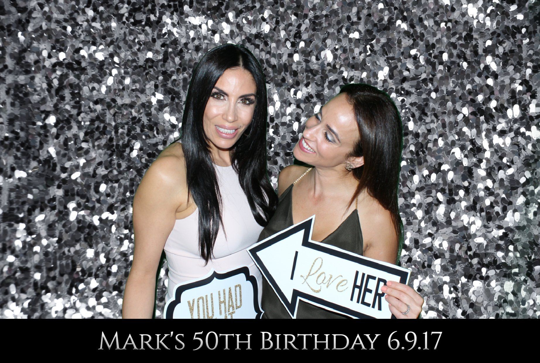 Two women are posing for a picture in a photo booth at a 50th birthday party.