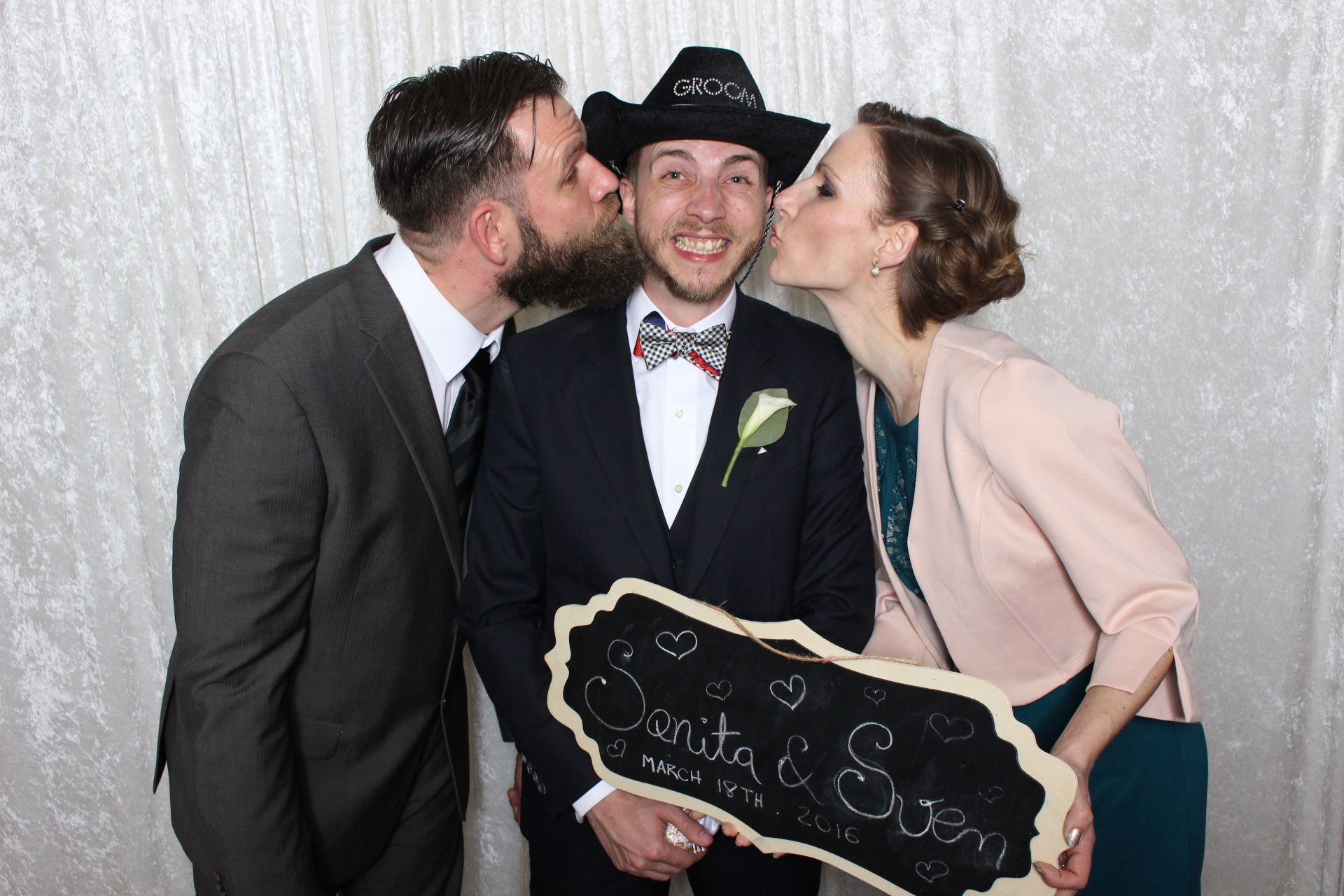 A man in a suit and cowboy hat is being kissed by two women.