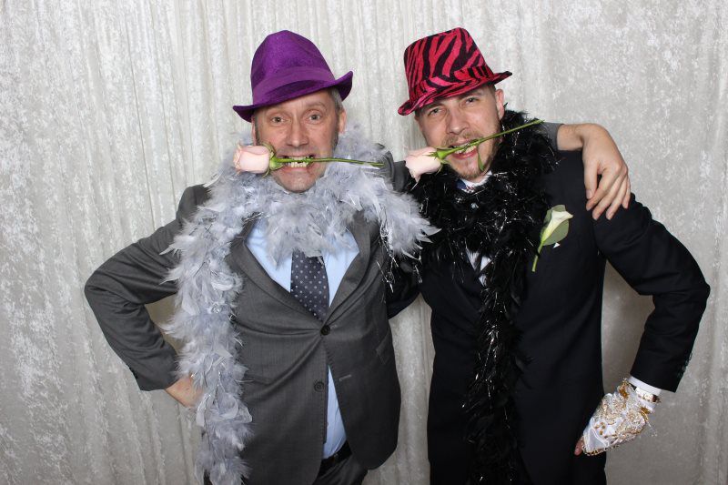 Two men in suits and hats are posing for a picture in a photo booth.