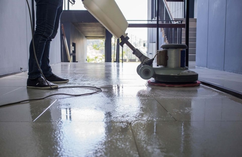 A Man Is Cleaning A Tiled Floor With A Machine — NJP Services In Shellharbour, NSW