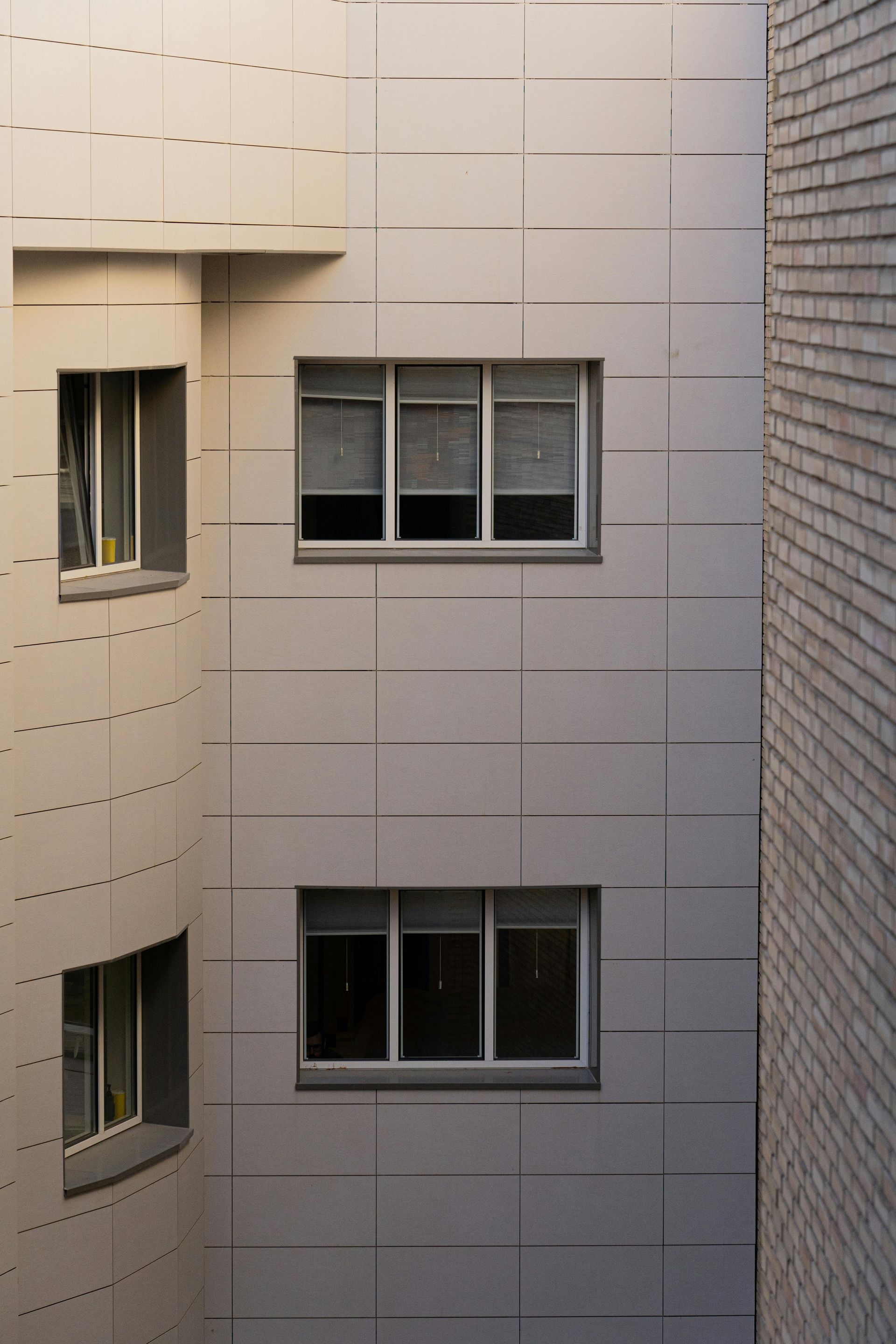 Building exterior with three rows of windows on a light-colored, textured wall; brick wall on the right.