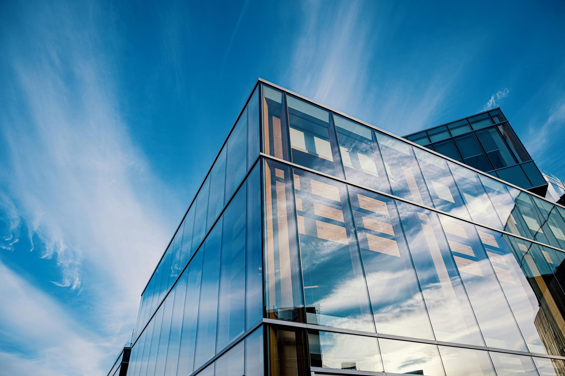 Modern glass building against a blue sky with cloud streaks.