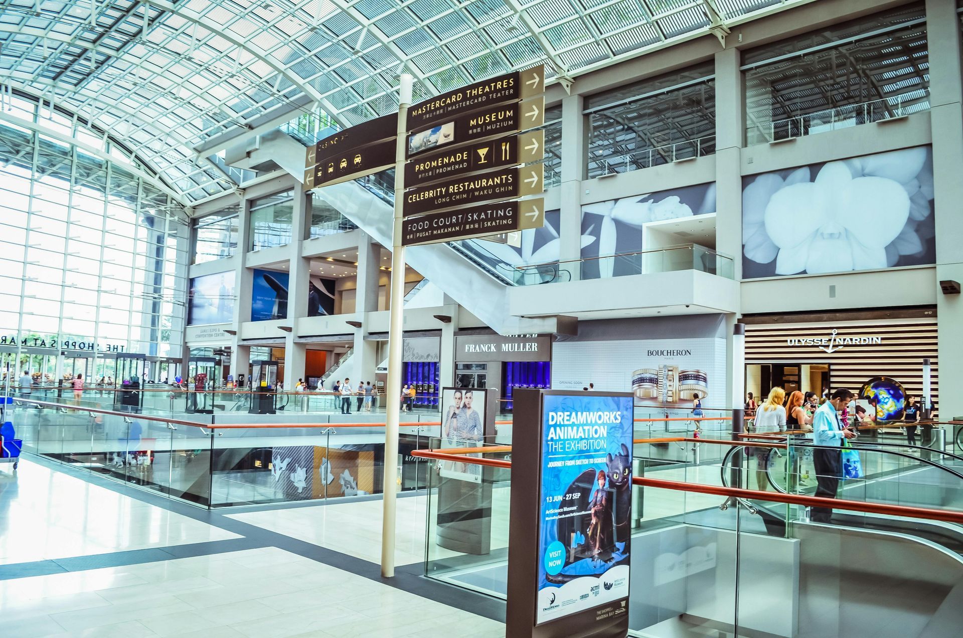 Interior view of a modern shopping mall with multiple levels, signs, and shoppers.