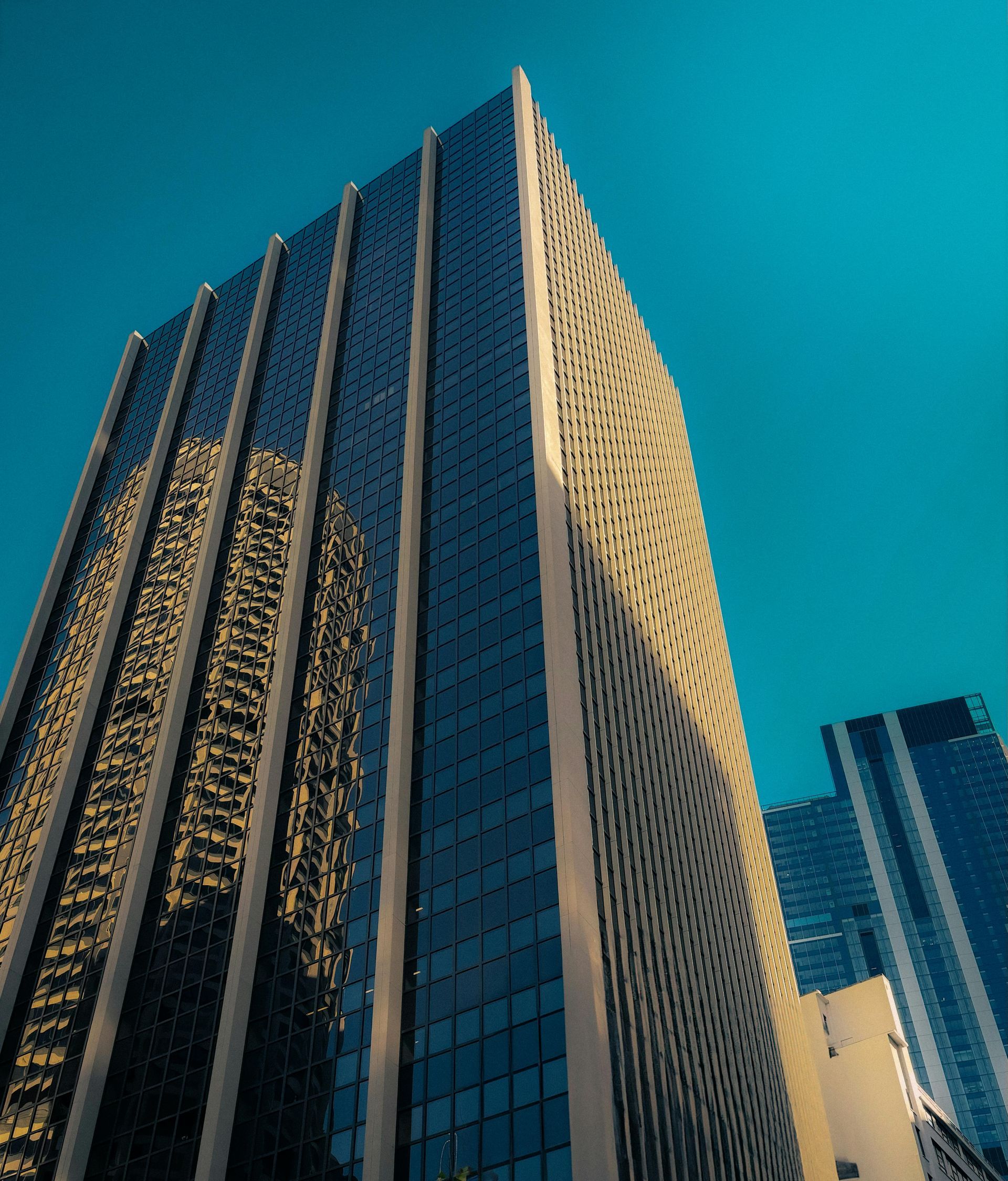 High-rise office building with reflective windows against a bright blue sky.Check icon