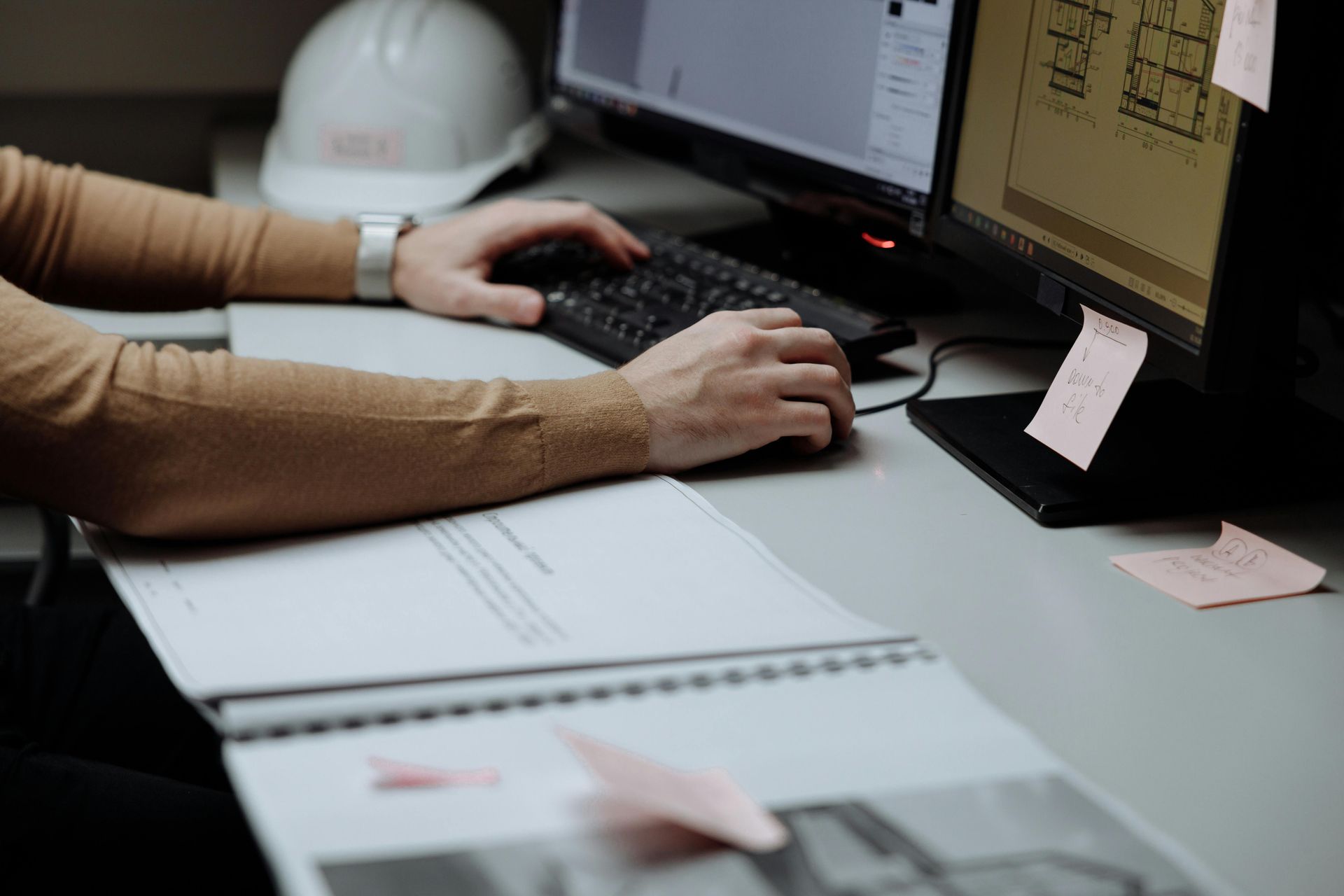 Person using a computer, with documents and a hard hat nearby.