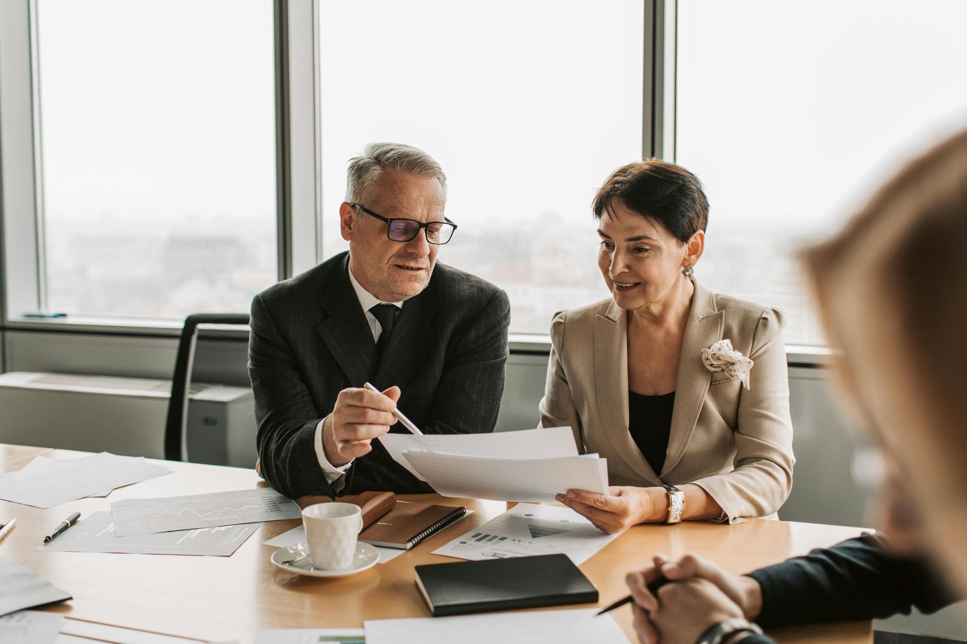 Businesspeople in a meeting, man pointing at document, woman looking, coffee cup, papers on table.