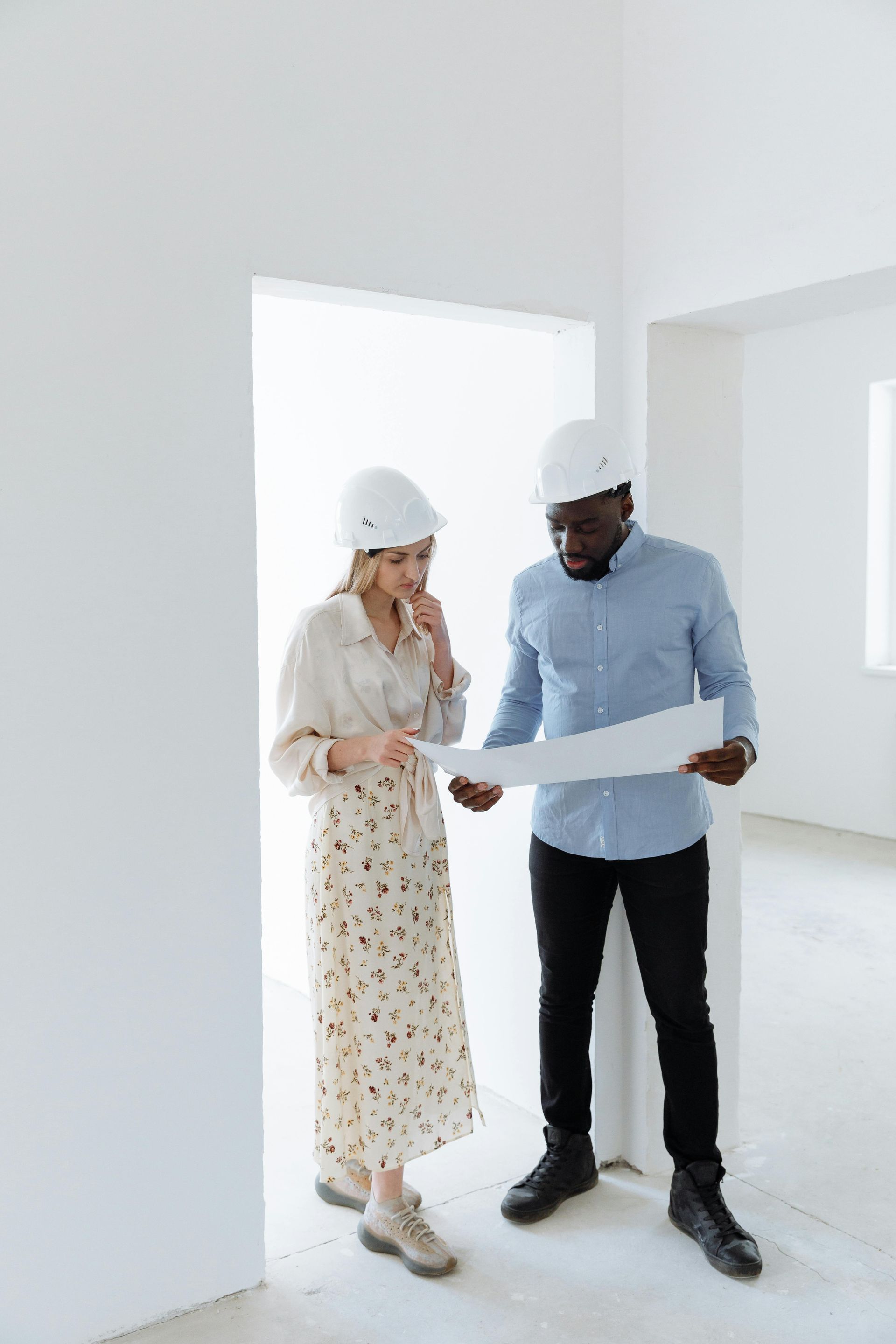 Two people in hard hats examining blueprints in a white room.