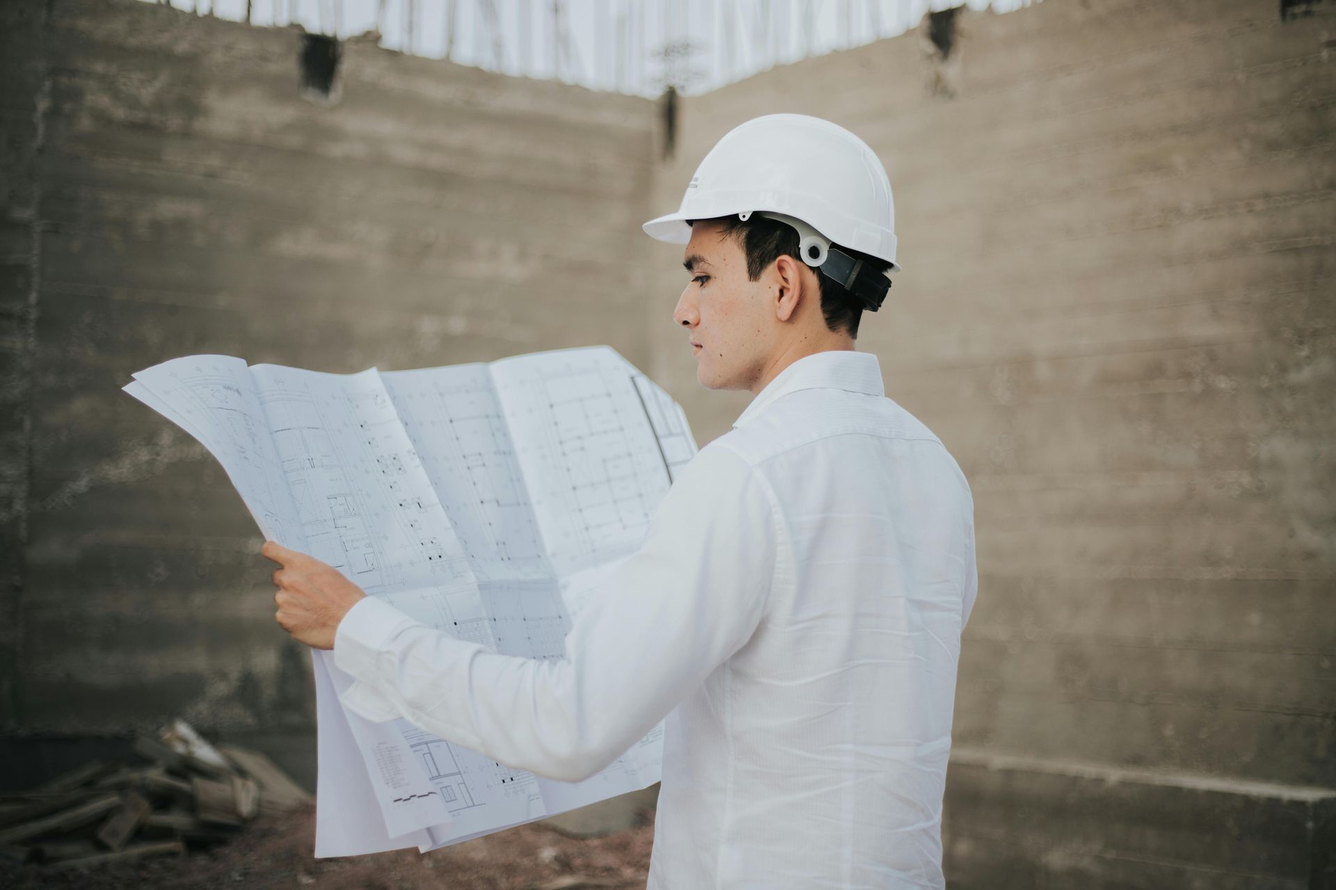 Construction worker in white hard hat and shirt studying blueprints at a construction site.