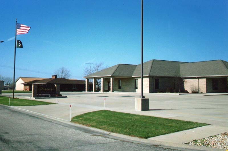 Exterior view of a single-story building complex with American flags, a sign, and a paved lot under a blue sky.