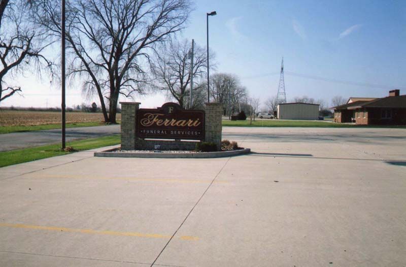 Sign for Ferrari Funeral Home in brown and gold, set in a concrete plaza.