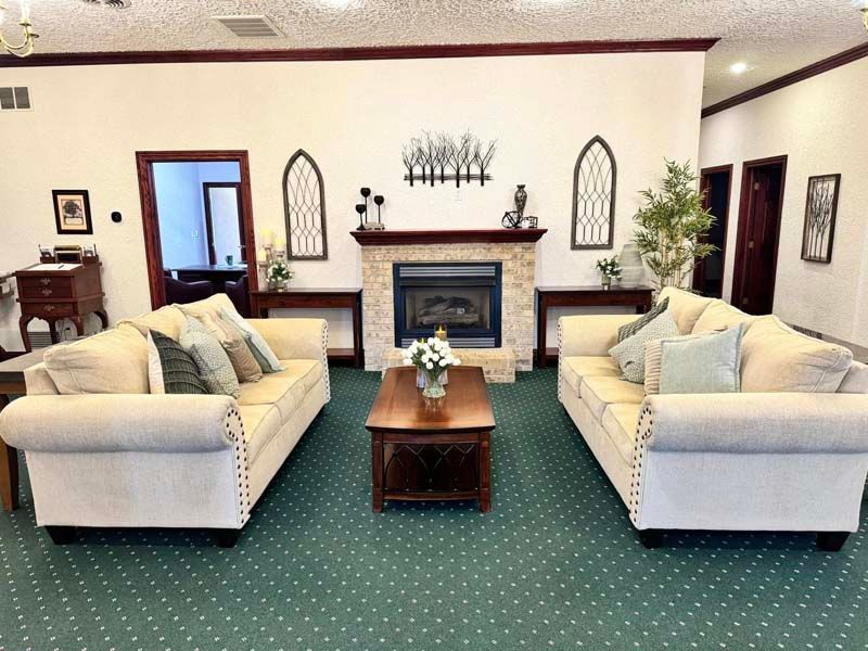 Cozy waiting room with two sofas, fireplace, coffee table, and green carpet.